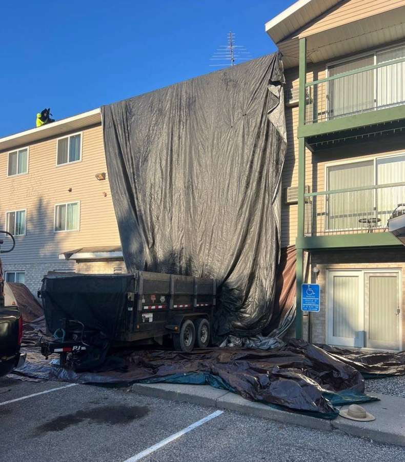 Debris trailer and tarps protecting a Hutchinson apartment building during tear-off, August 2024