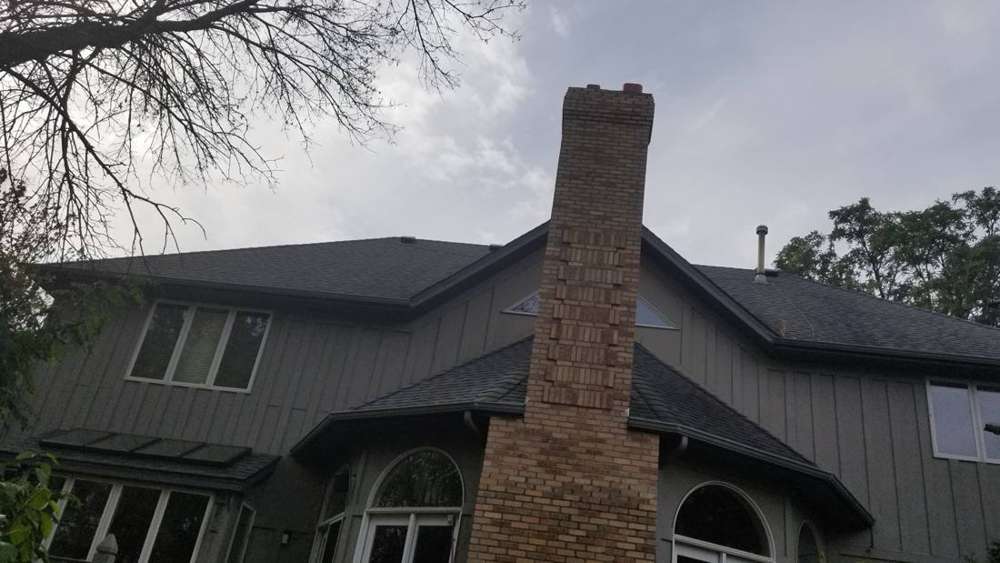Tall brick chimney rising above the dark shingle roof of a two-story Champlin, MN home, October 2018