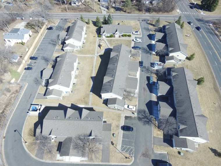 Drone view looking down on a Maplewood, MN townhome community with gray shingle roofs, parking courts and a curving street, photographed by Repair King