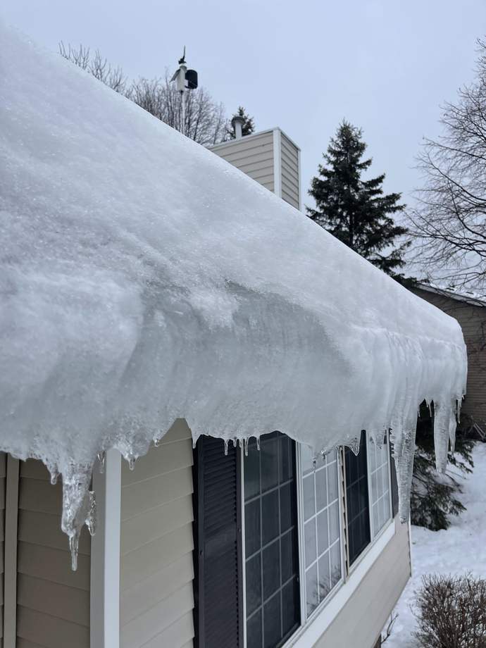 Thick sheet of ice curling off the eave of a Minnesota home, photographed by Repair King