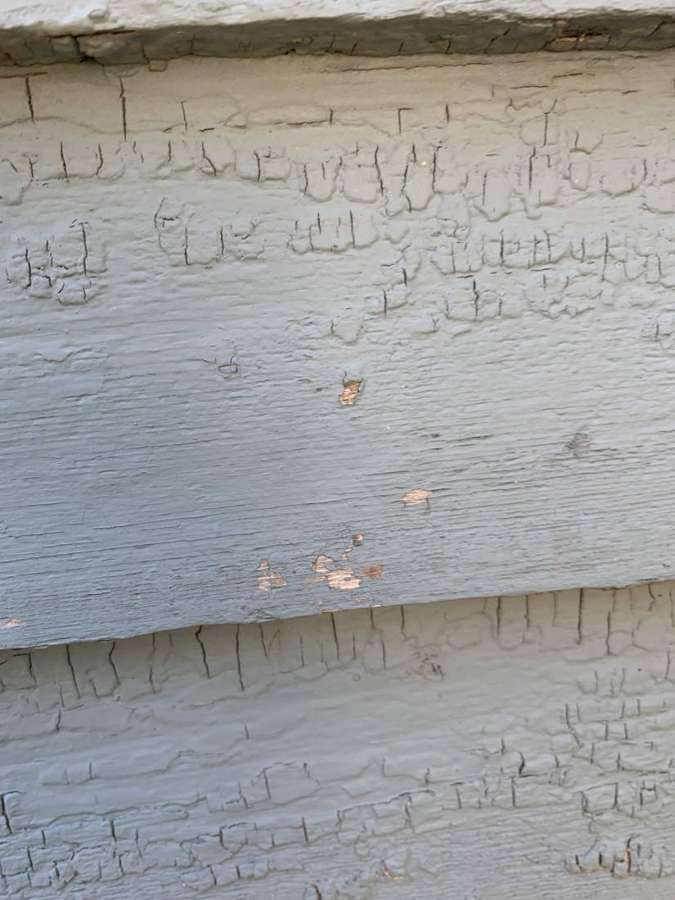 Peeling and cracked paint on wood clapboard siding in Watertown