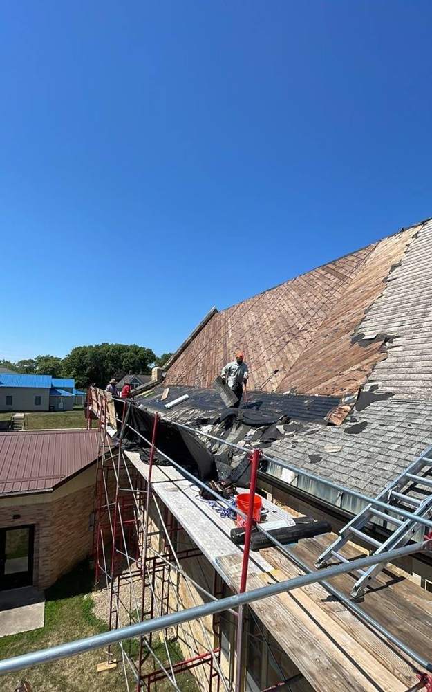 Repair King crew tearing off the roof beside the stone bell tower of St. Paul Lutheran Church in St. James, MN, July 2023