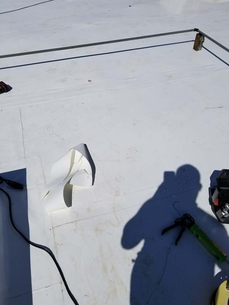 A piece of white PVC flashing being fitted on the new Duro-Last membrane, with a caulk gun and tools nearby, on the Forest Lake Chrysler Jeep Dodge roof in Forest Lake, MN