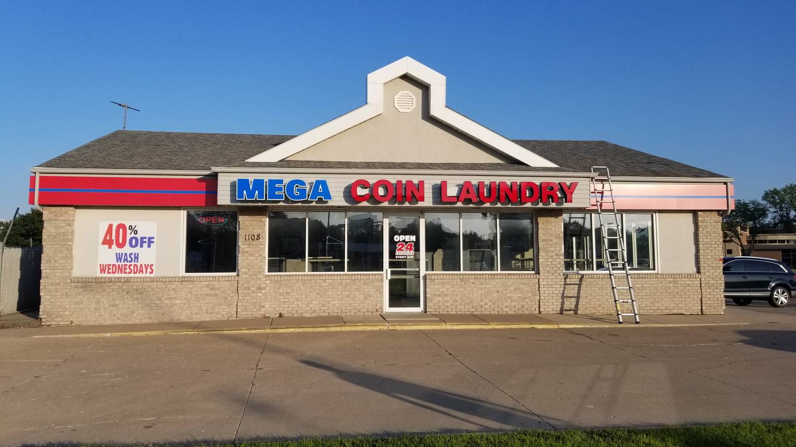 Mega Coin Laundry on East Blue Earth Avenue in Fairmont, MN, a one-story brick and stucco building with a gable roof, with ladders up during a Repair King roof inspection