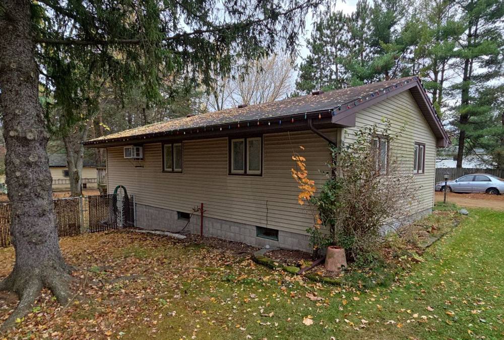 Single-level vinyl-sided home with a brown shingle roof among tall pines in the Forest Lake, MN area, photographed by Repair King in October 2025