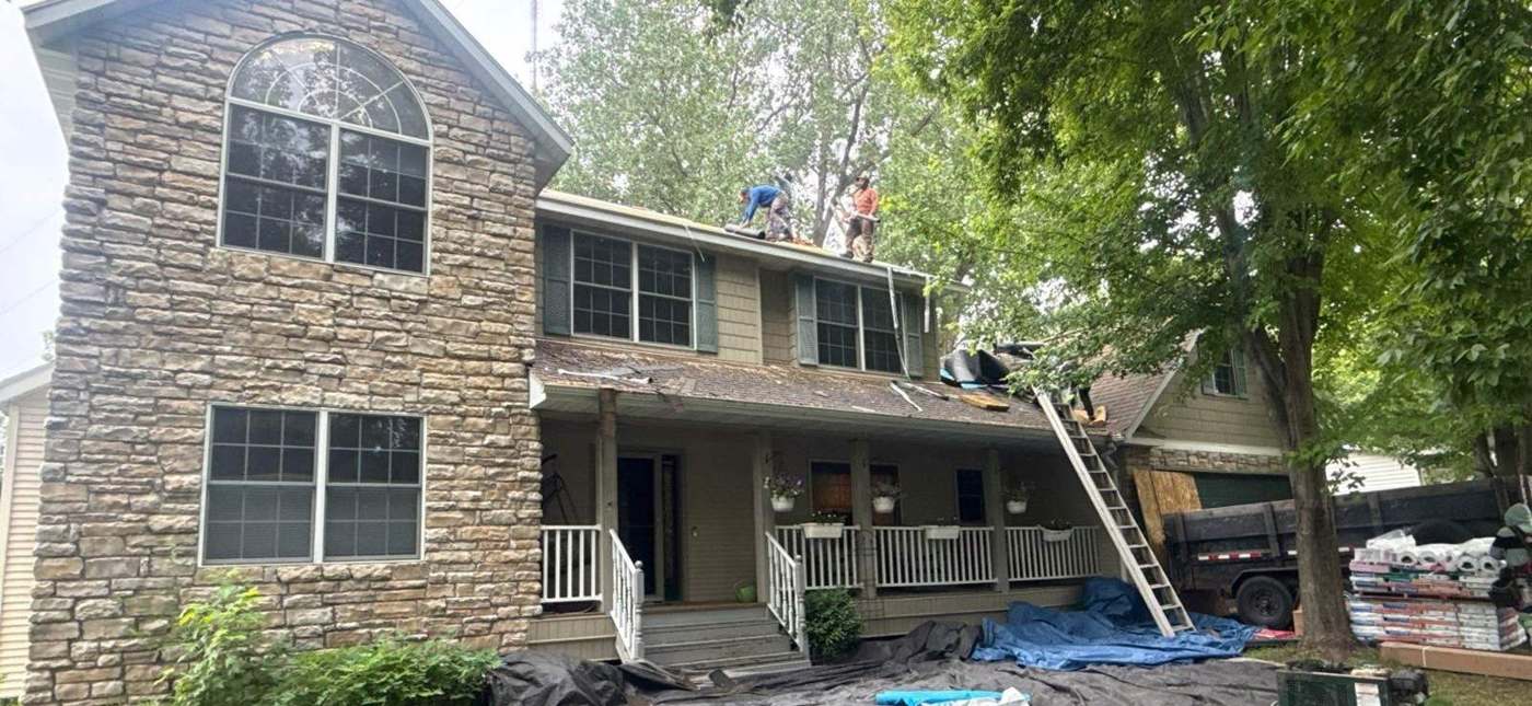 Repair King crew tearing off the roof of a stone-front two-story home on Suzanne Avenue in Shoreview, MN, with tarps protecting the yard, June 2026