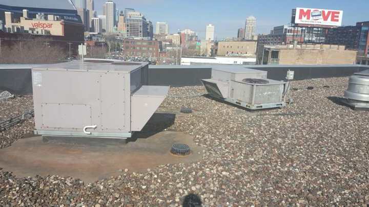 Rooftop HVAC units on the river-rock ballasted flat roof of Bobby & Steve's Auto World on Washington Avenue in downtown Minneapolis, with the skyline behind