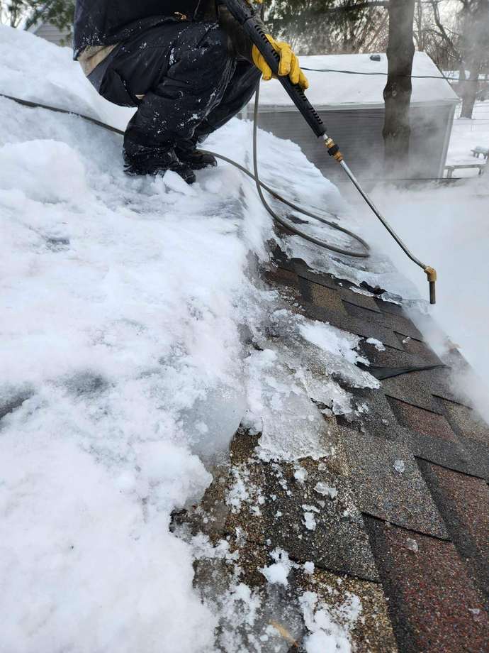 Repair King technician using a low-pressure steam wand to melt an ice dam off asphalt shingles