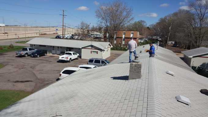 Repair King crew walking the long shingle roofs of Red Rock Lodge in Newport, MN, above the parking lot