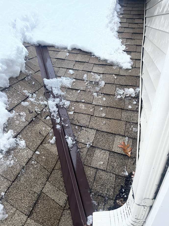 Clean drainage channel steamed through ice and snow along an eave and gutter