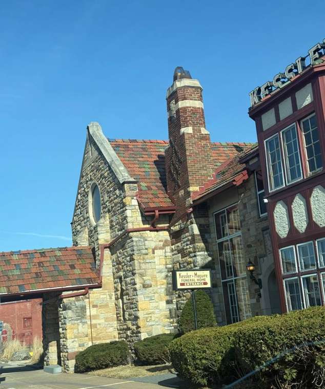 Kessler & Maguire Funeral Home on West 7th Street in St. Paul, a stone building with a multicolored clay tile roof and brick chimney, March 2025