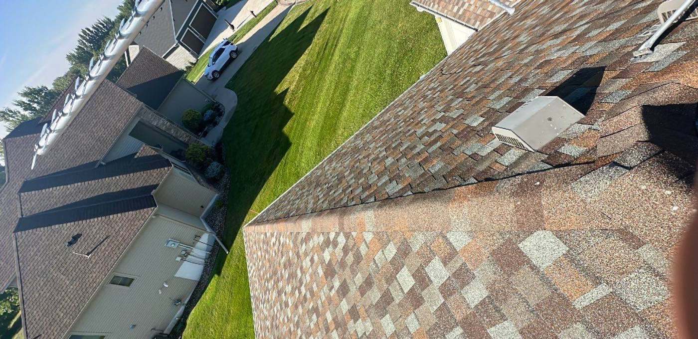 View across a steep shingle roof toward the neighboring homes during a Repair King inspection in Annandale, MN, July 2023