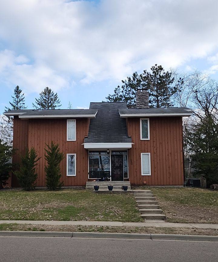 Two-story home with vertical wood siding and a steep dark shingle center roof on Folwell Avenue in Falcon Heights, MN, April 2023