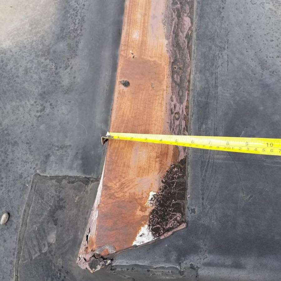 A rusted metal strip measured with a tape on the flat roof at 1111 S. Robert St.