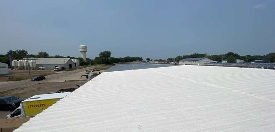 Low-slope roof of The Marketplace grocery store in Cokato, MN, with the town water tower in the background, July 2023