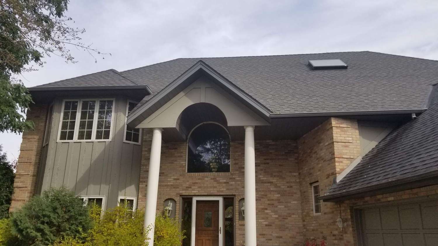 Two-story Champlin, MN home with brick, gray board-and-batten siding, white columns and an arched window, photographed by Repair King in October 2018