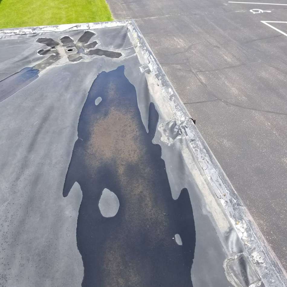A long pool of standing water along the edge of the flat rubber roof at King of Glory Lutheran Church in Blaine, MN, July 2017
