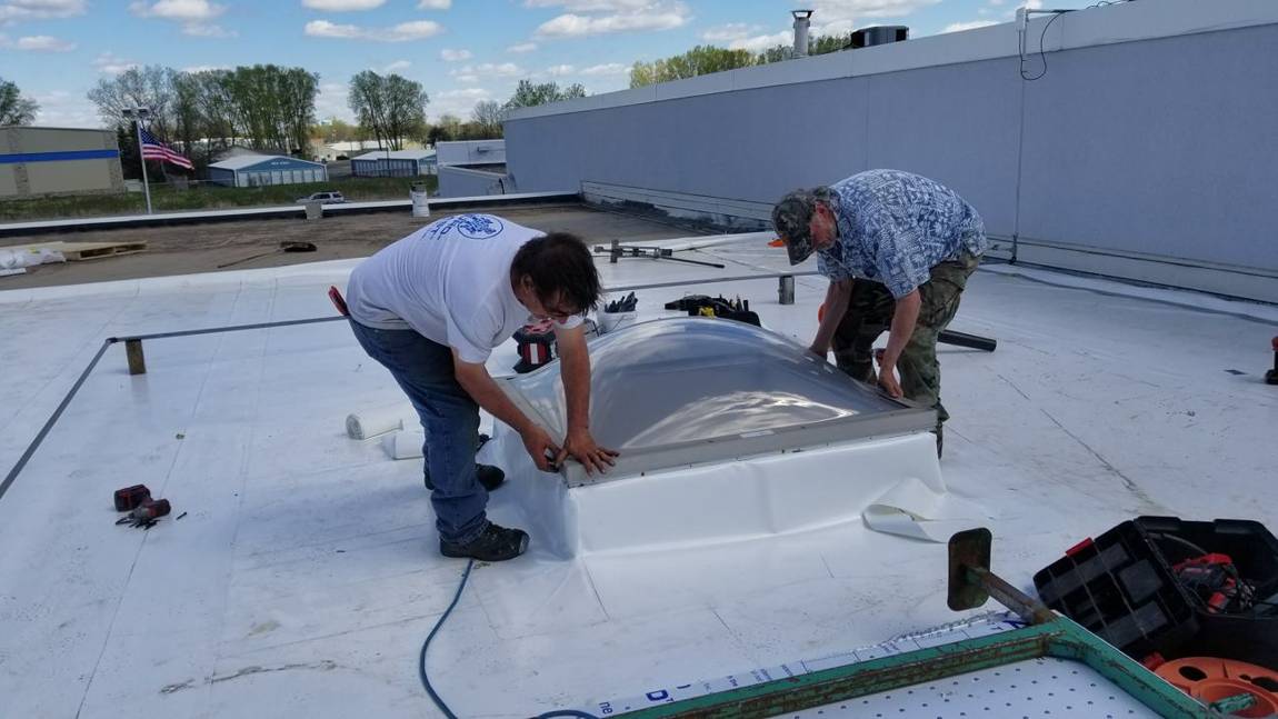 Repair King crew flashing a domed skylight curb with white PVC membrane on the Forest Lake Chrysler Jeep Dodge flat roof in Forest Lake, MN