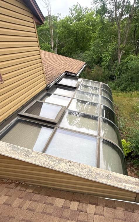 Glass-roofed sunroom beside the shingle roof on a Stacy home, June 2026