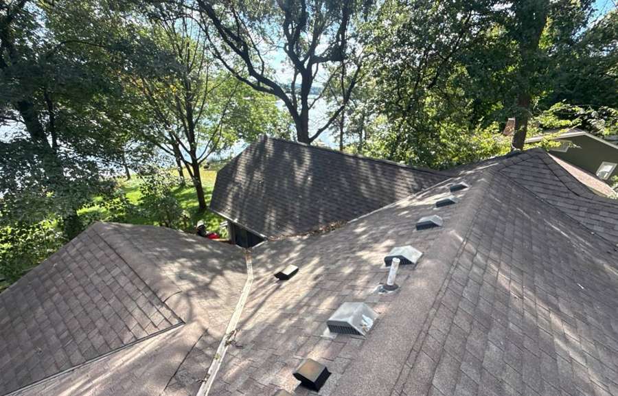 Shaded roof with box vents and an open valley on a River Acres Road home in Cottage Grove, Mississippi River visible through the trees, September 2025