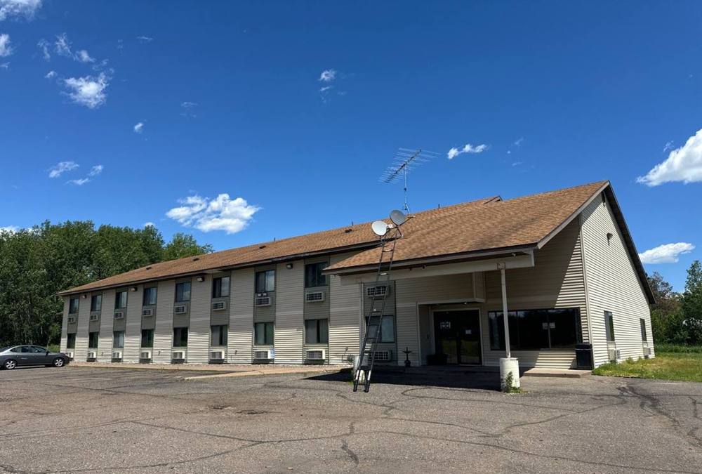 Two-story motel with a brown shingle roof and tan siding on MN-23 in Finlayson, MN, with a ladder at the entry during a Repair King roof inspection, June 2024