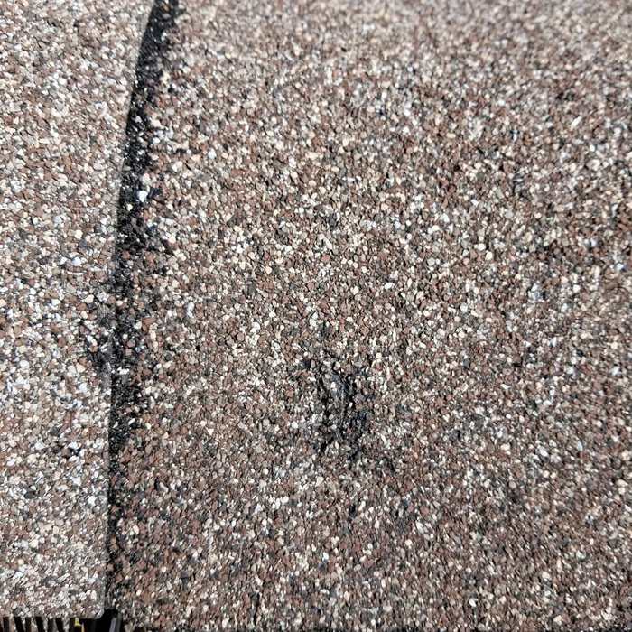 Close-up of a bruise with granule loss on an architectural shingle, photographed during a Hugo storm inspection