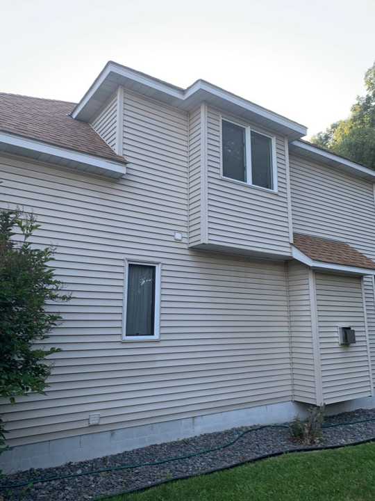 Side wall of the Plymouth home with vinyl siding and a two-story gable, August 2019