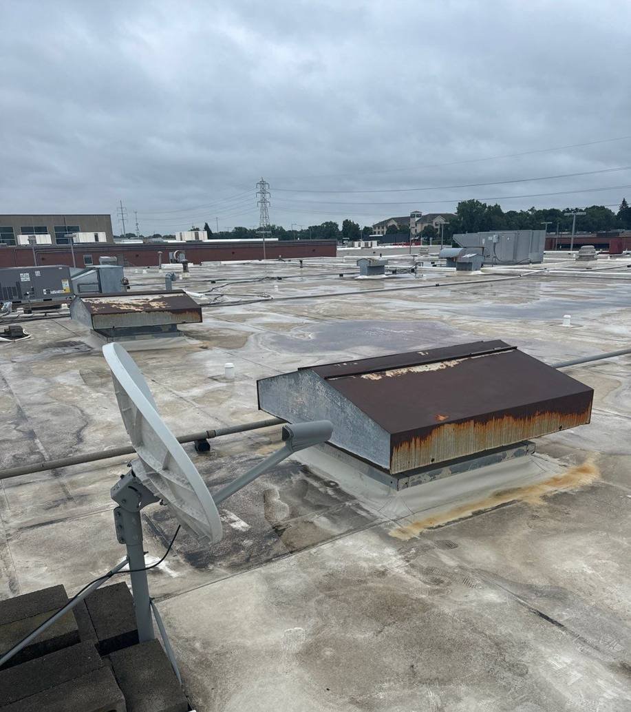 Worn membrane, rooftop hatch and satellite dish on the Bloomington Lincoln roof before replacement, July 2024