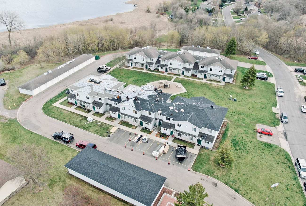 Aerial view of Repair King's re-roof of the Waters Edge townhomes on Shoreline Drive in Howard Lake, MN, with Howard Lake visible behind the buildings, April 2024