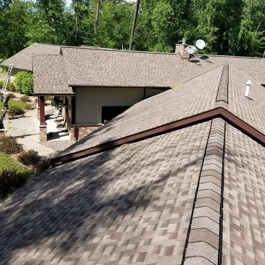 Brown architectural shingle roof and ridge caps on a large ranch home on a wooded lot in Hugo, MN, photographed from the roof during a Repair King inspection