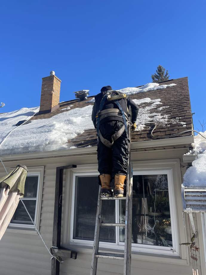 Repair King crew member in a safety harness on a ladder at a snowy roof edge