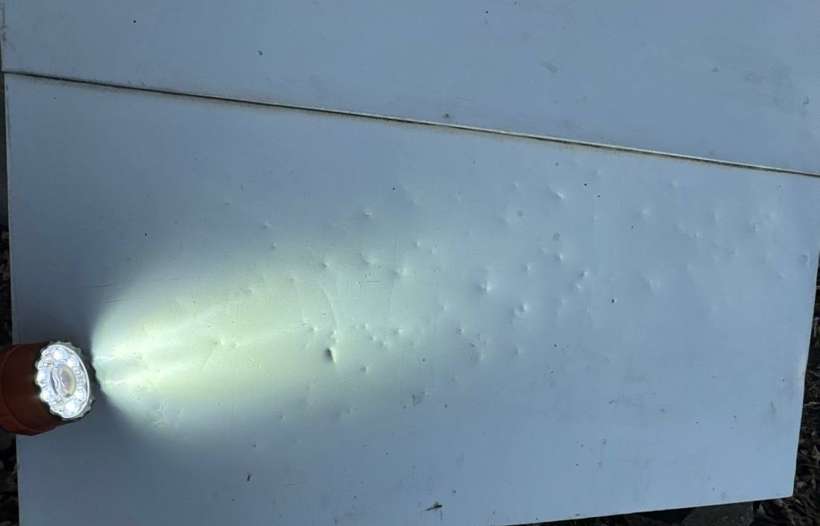 A flashlight held flat against vinyl siding shows rows of small dents, Little Falls-area farmhouse, January 2024