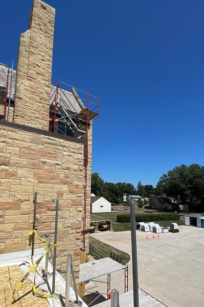 Stone wall and chimney of St. Paul's Lutheran Church in St. James, MN, with scaffolding and guardrails during Repair King's July 2023 re-roof