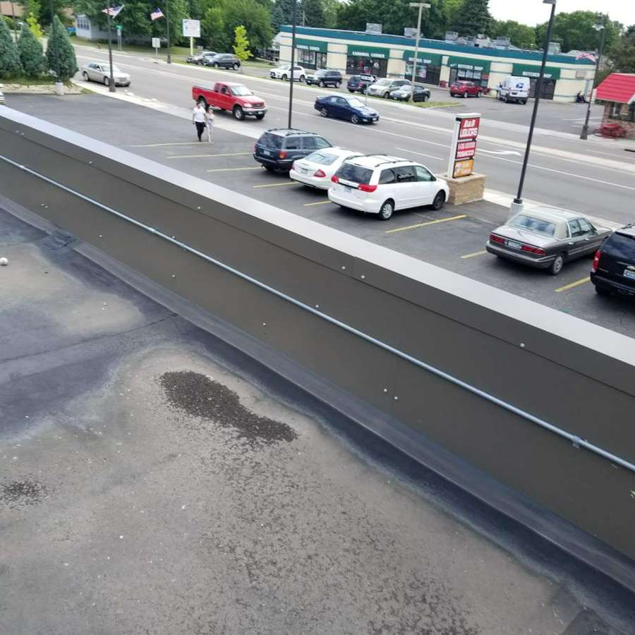 View from the flat roof edge of a West St. Paul strip center looking down at the parking lot and traffic on South Robert Street