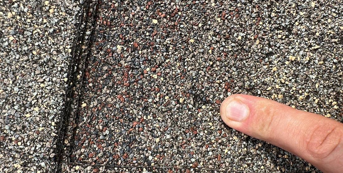 Hail hit pointed out on a Hopkins asphalt shingle during a roof inspection, August 2023