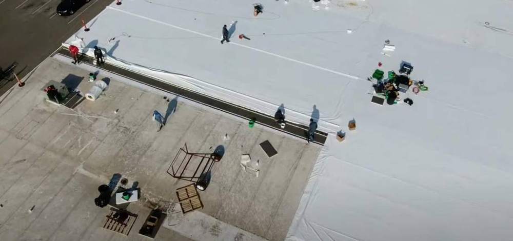 Drone view of Repair King crews installing new white membrane on The Marketplace grocery store roof in Cokato, July 2024