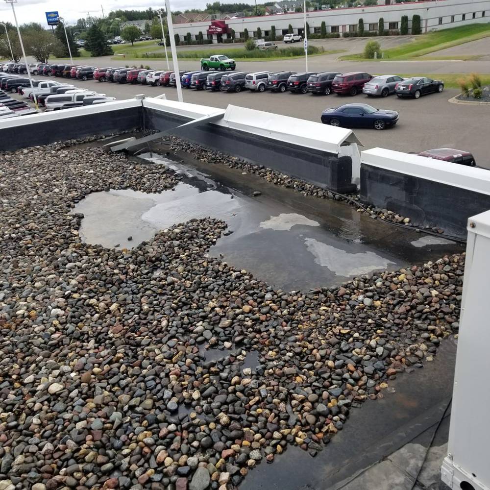 Ponding water on the old gravel roof along the parapet wall at Forest Lake Chrysler Jeep Dodge