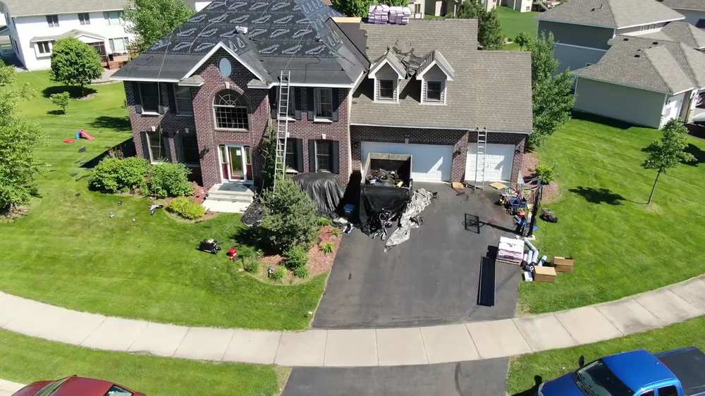 Brick two-story home in Brooklyn Park mid-reroof, tear-off debris going straight into the trailer