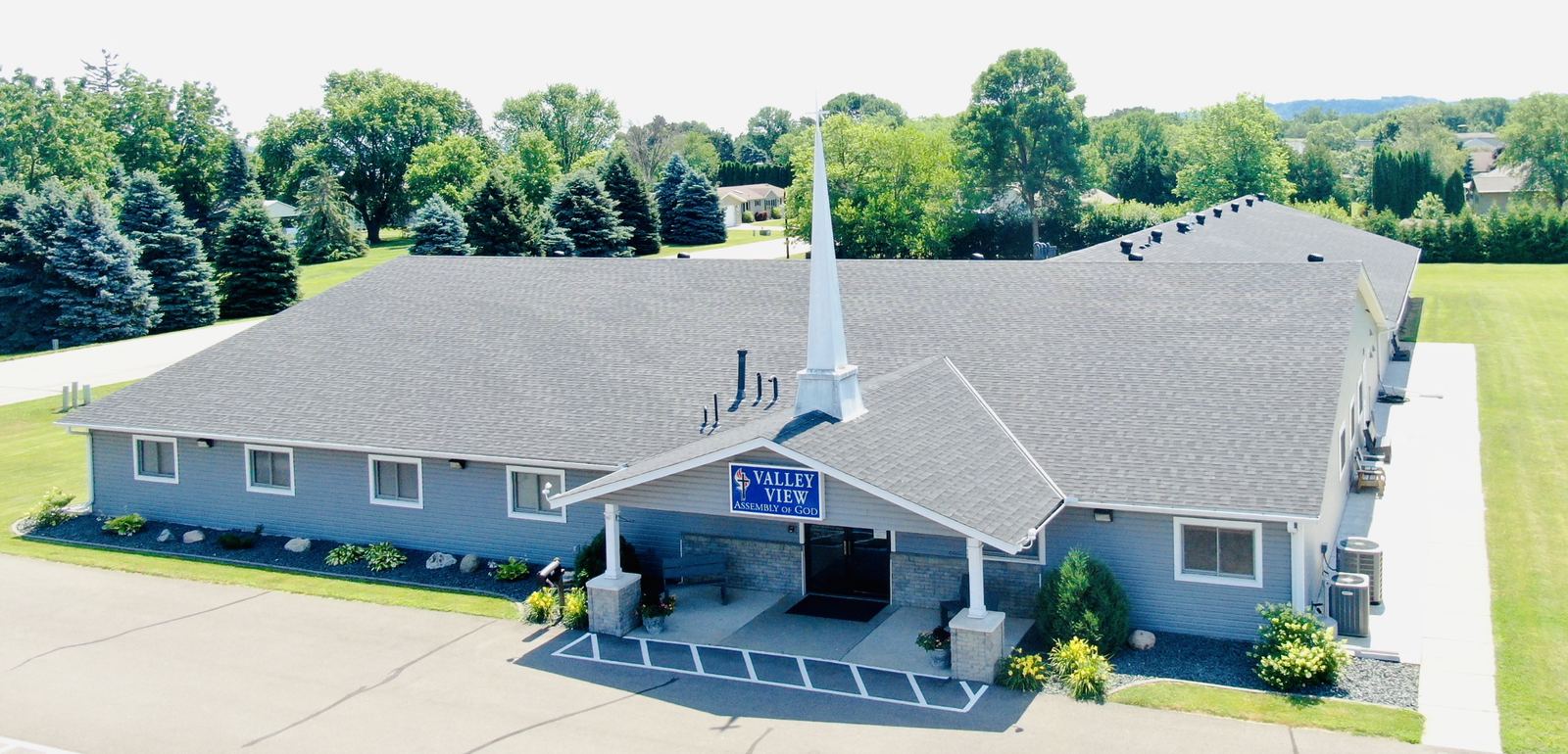 Drone view of Valley View Assembly of God in Lake City, MN, with its new gray shingle roof, white steeple and blue siding, completed by Repair King
