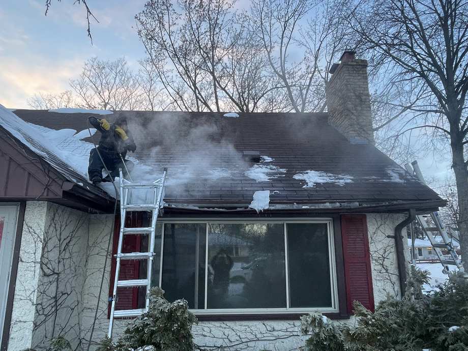 Crew member steaming an ice dam off a roof with steam rising