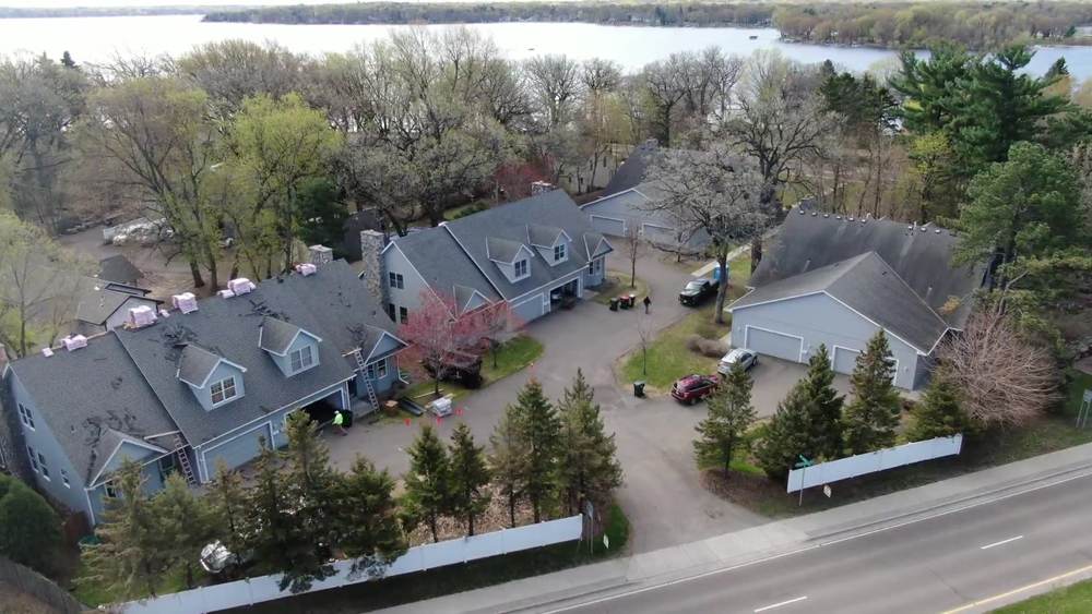 Drone view of townhome buildings with shingle bundles staged on the ridges and the lake behind them in White Bear Lake, MN