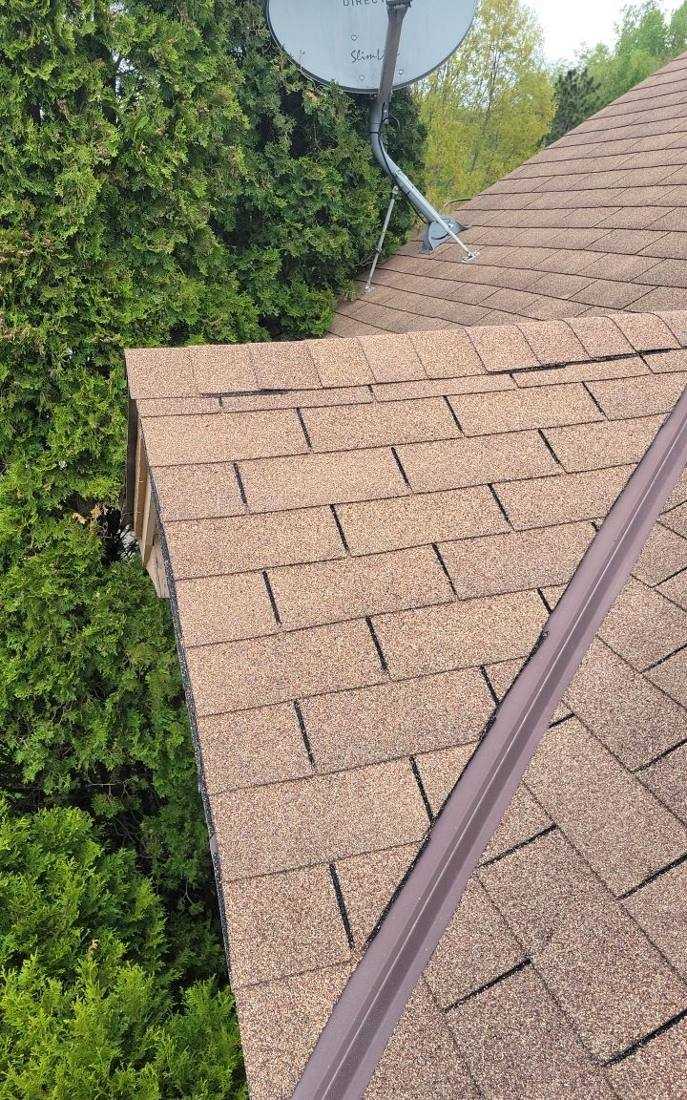 Cracked shingle and satellite mount found on an Oakdale roof close to the tree line, May 2022
