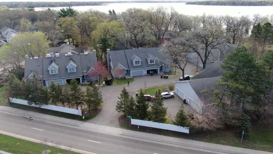 Drone view of a gray townhome community with shingle bundles staged along the ridges and the lake behind it in White Bear Lake, MN, a Repair King multifamily roofing project