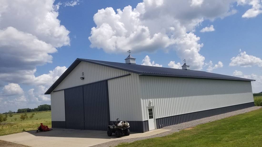 White steel pole building with a dark roof, cupola and sliding doors on a farm near Blue Earth, MN