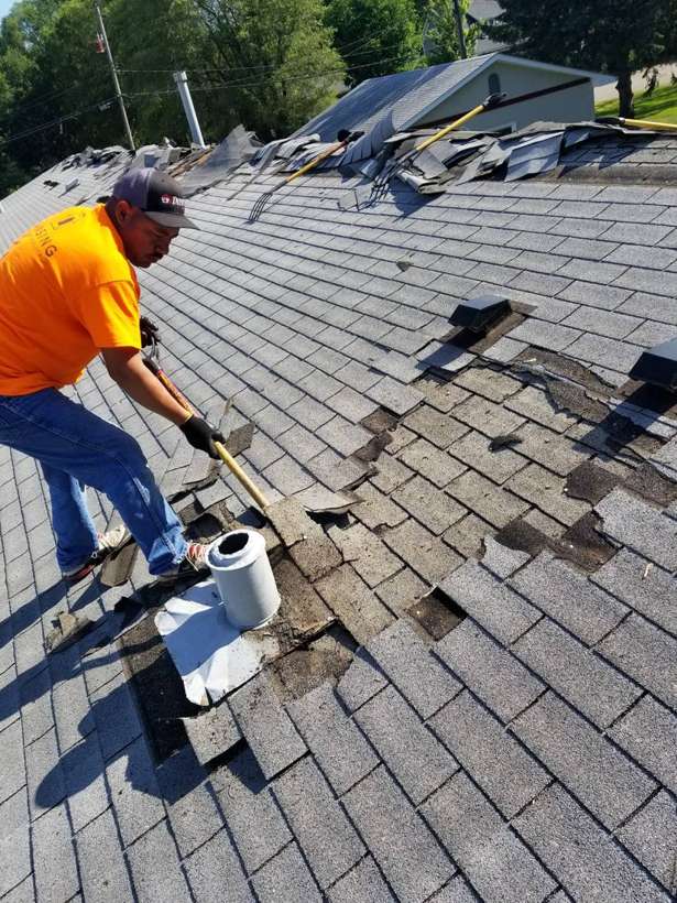 Repair King crew member tearing off old shingles around a roof vent at Red Rock Lodge in Newport, MN