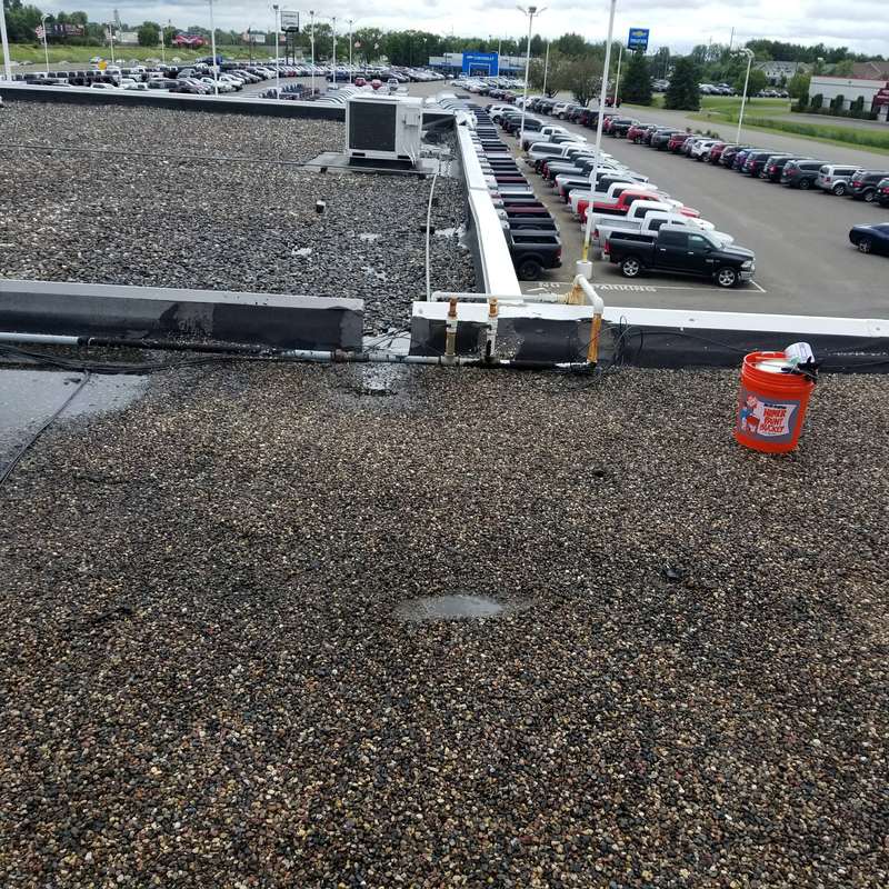 Rooftop equipment runs across the old gravel roof above the dealership lot in Forest Lake