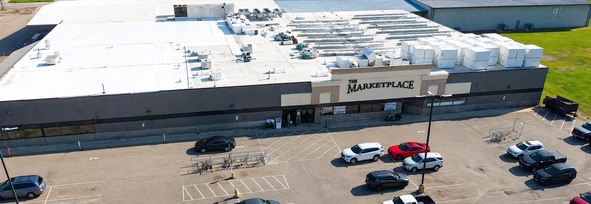 Retail grocery center with a white flat commercial roof and rooftop units, aerial photo
