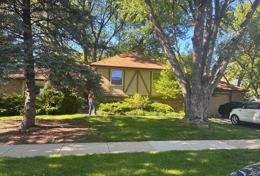 Tudor-style home tucked among mature trees in Naperville, photographed during a roof project, May 2026