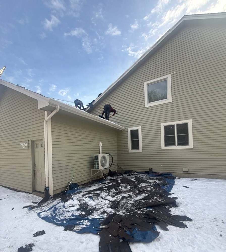 Tear-off debris on a snowy lawn beside a two-story home during a Repair King re-roof in Chanhassen, MN, December 2025