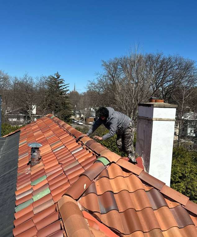 Repair King crew member working on a red clay barrel-tile roof beside a white chimney on West Summit Avenue in St. Paul, March 2025